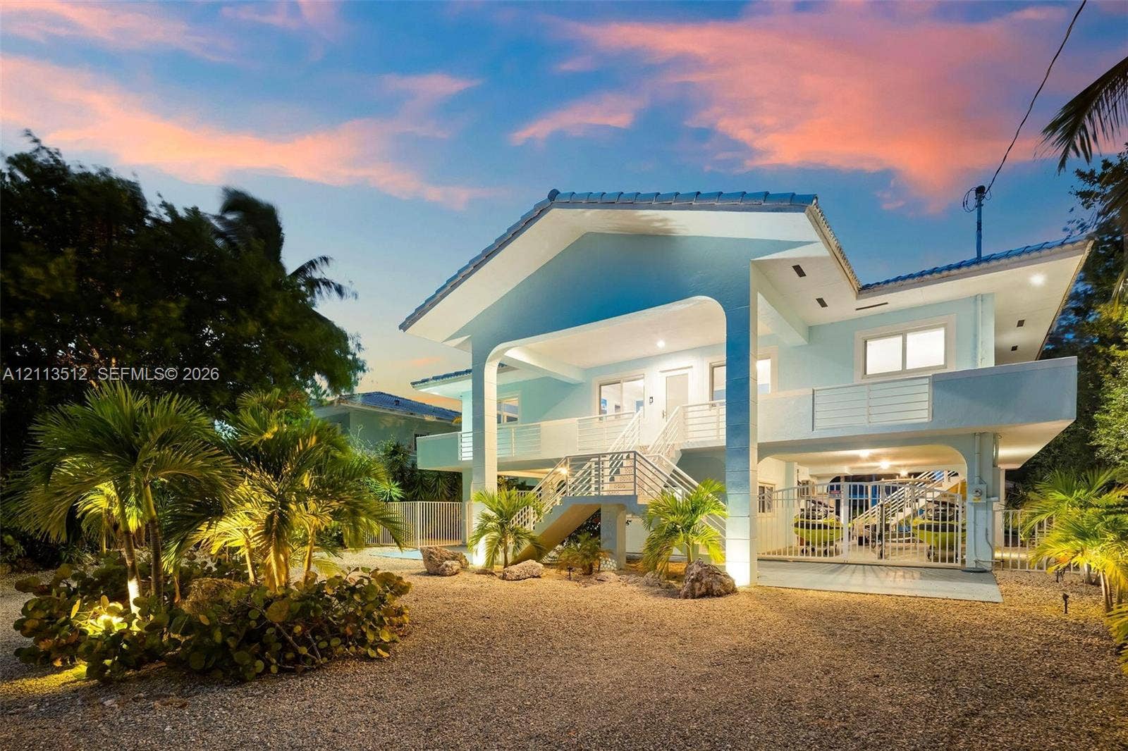 Key Largo, FL 33037 Elevated multi-story residence featuring a covered entryway, dual-level railed balconies, and a gravel ground-level exterior