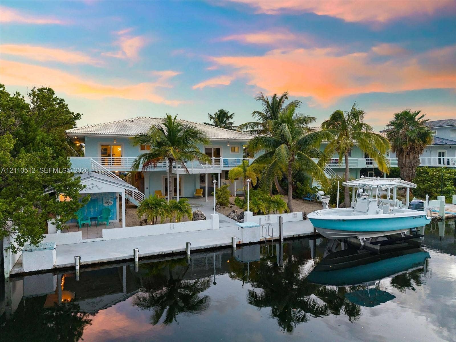 Key Largo, FL 33037 Waterfront property featuring a private boat dock with lift, concrete seawall, covered patio space, and two-story exterior balcony