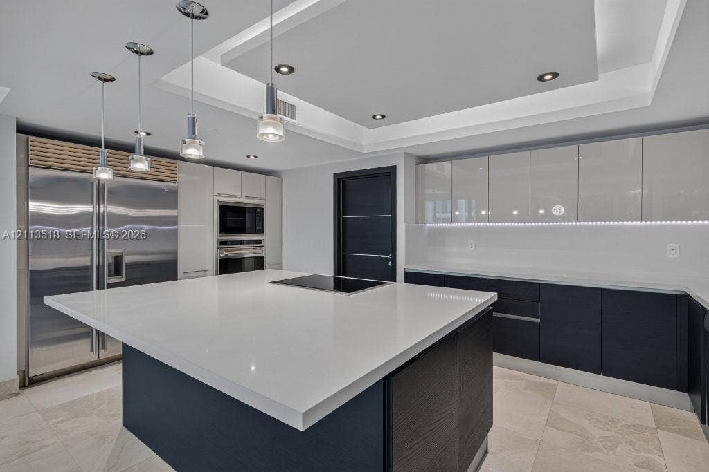 3131 NE 188th Street, #1-303, Aventura, FL 33180 Contemporary kitchen featuring a spacious center island with a stone countertop, high-gloss cabinetry, stainless steel professional-grade appliances, recessed ceiling lighting, and tile flooring