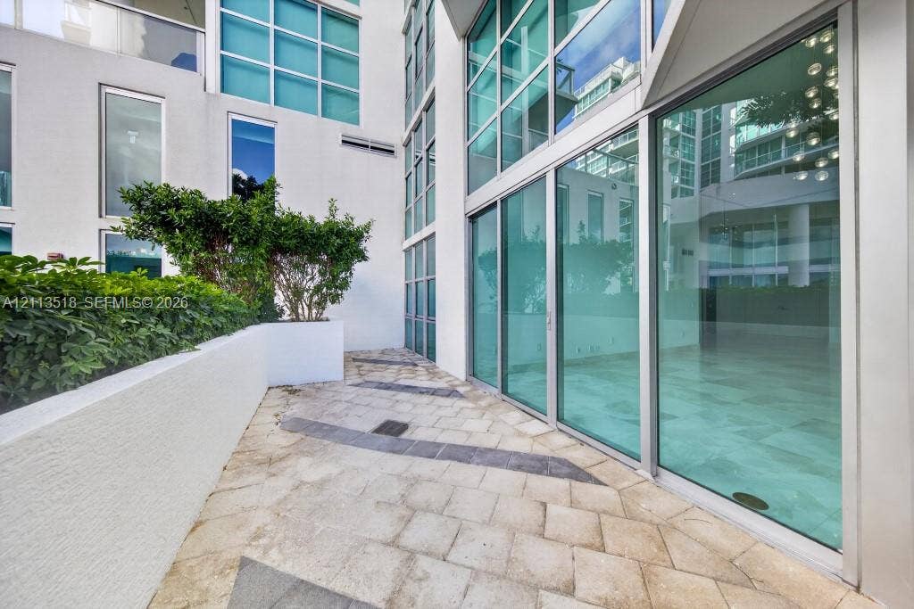 3131 NE 188th Street, #1-303, Aventura, FL 33180 Private terrace featuring large-format stone pavers, integrated concrete planter beds with mature shrubbery, and floor-to-ceiling glass wall panels with metal frames