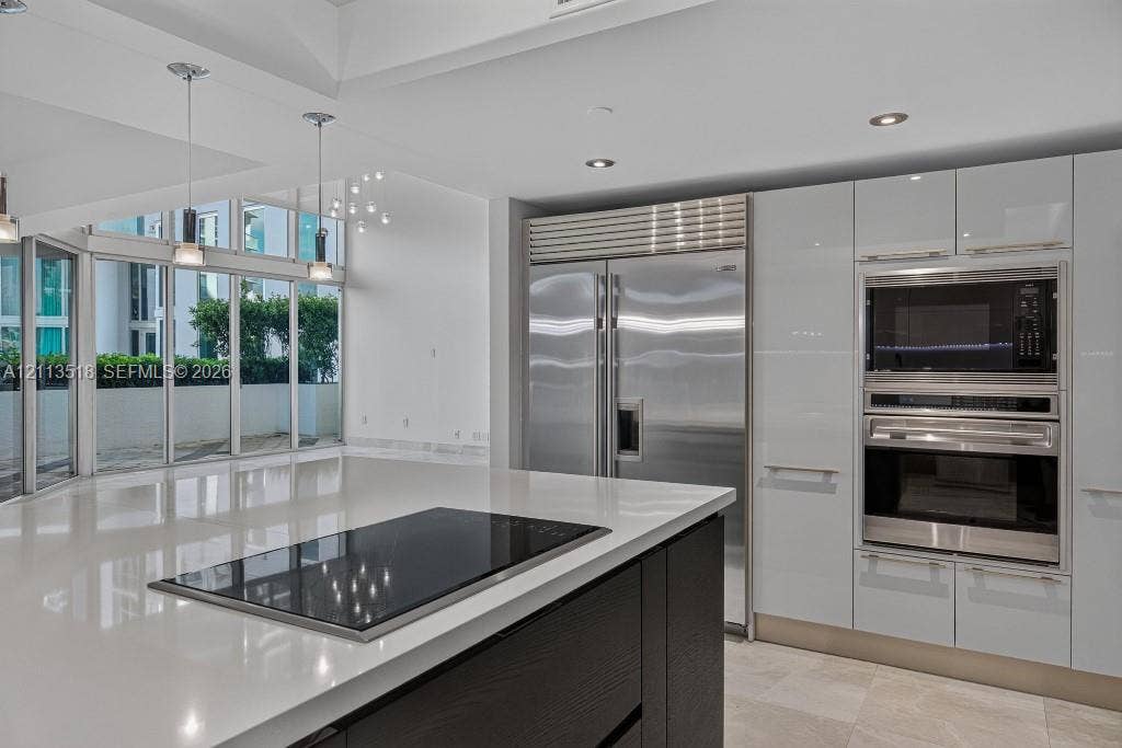 3131 NE 188th Street, #1-303, Aventura, FL 33180 Kitchen featuring high-gloss cabinetry, a large central island with an integrated cooktop, stainless steel professional-grade appliances, recessed lighting, and floor-to-ceiling windows