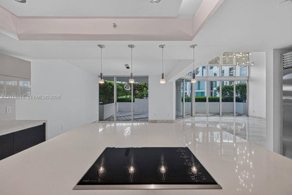3131 NE 188th Street, #1-303, Aventura, FL 33180 Kitchen island featuring a solid surface countertop, built-in induction cooktop, four pendant light fixtures, and multi-panel floor-to-ceiling glass sliding doors