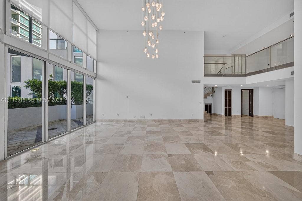 3131 NE 188th Street, #1-303, Aventura, FL 33180 Expansive interior space featuring double-height ceilings, floor-to-ceiling windows, polished stone flooring, a multi-pendant light fixture, and a mezzanine level with glass railings