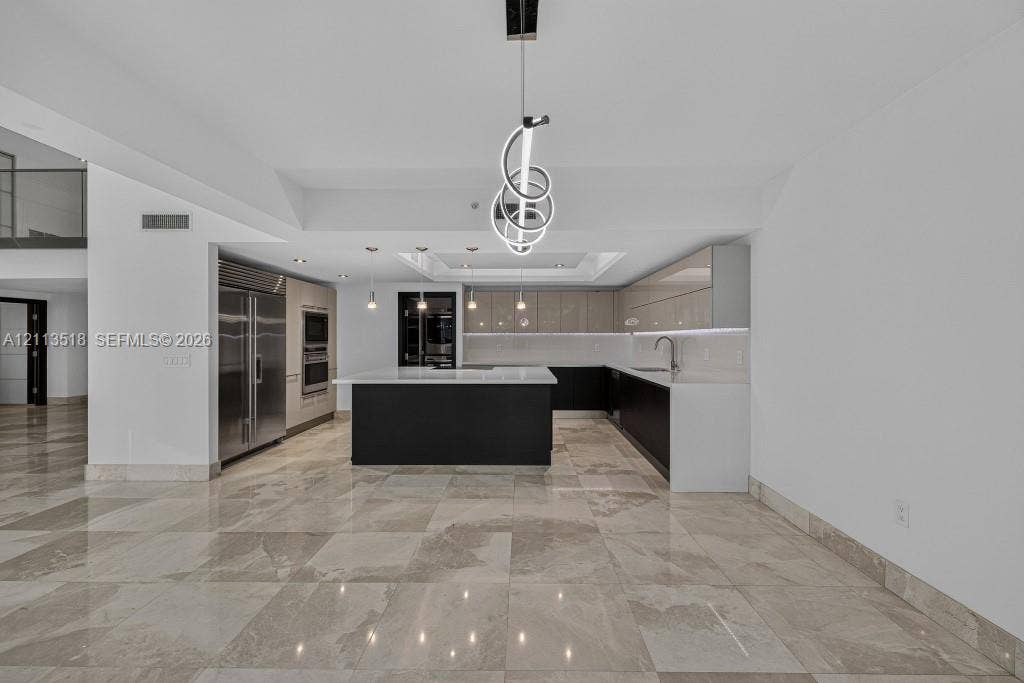 3131 NE 188th Street, #1-303, Aventura, FL 33180 Kitchen featuring high-gloss cabinetry, stone countertops, central island, integrated stainless steel appliances, and large-format tile flooring