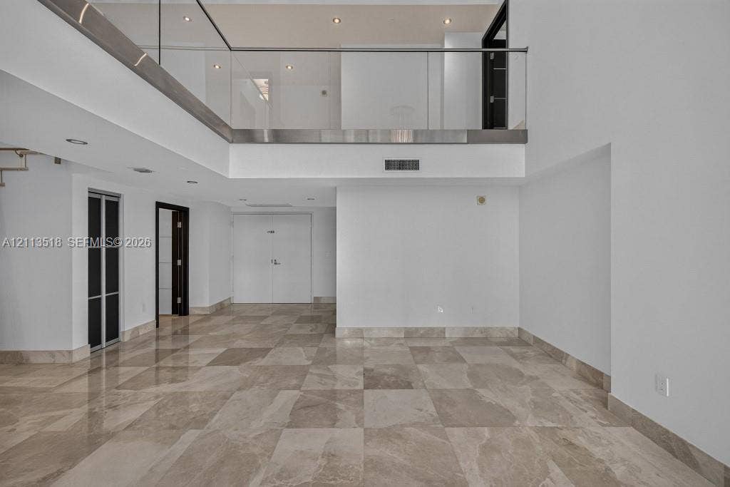 3131 NE 188th Street, #1-303, Aventura, FL 33180 Interior space featuring high ceilings, polished stone flooring, a glass-panel mezzanine railing, recessed lighting, and multi-panel doors