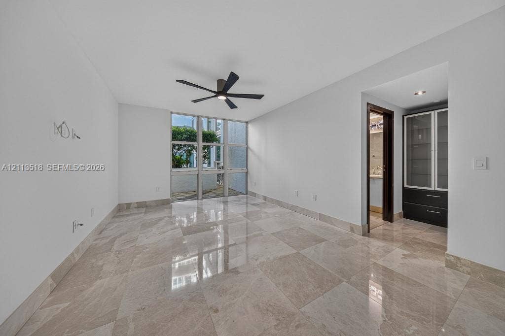 3131 NE 188th Street, #1-303, Aventura, FL 33180 Interior space featuring large-format stone tile flooring, floor-to-ceiling windows, a ceiling fan with integrated lighting, and built-in cabinetry with glass-front uppers