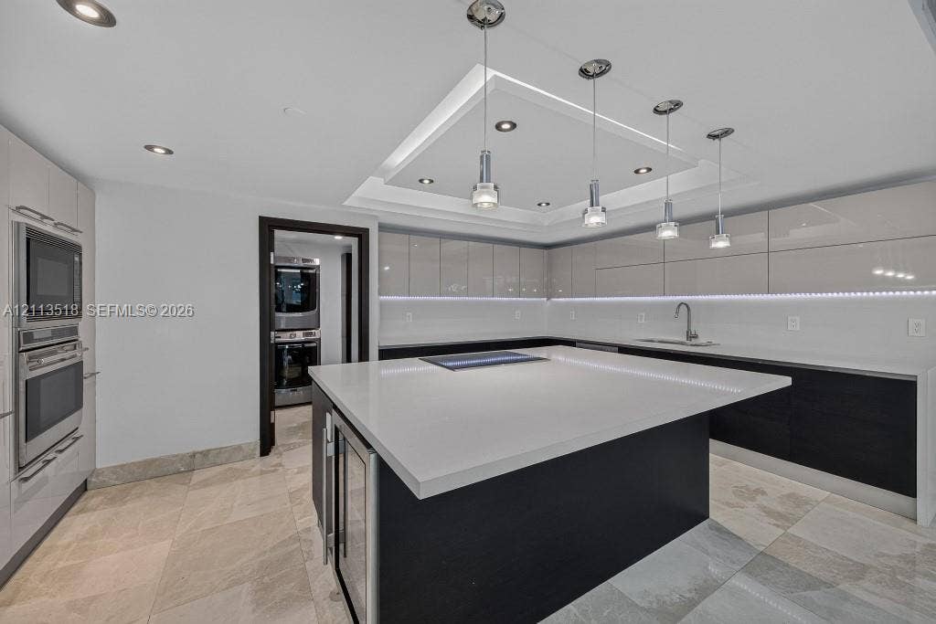 3131 NE 188th Street, #1-303, Aventura, FL 33180 Kitchen featuring high-gloss cabinetry, a central island with a solid-surface countertop, recessed tray ceiling lighting, stainless steel built-in appliances, and tile flooring