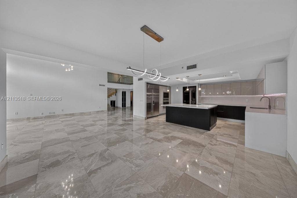 3131 NE 188th Street, #1-303, Aventura, FL 33180 Open-concept interior featuring large-format tile flooring, a kitchen island with a neutral countertop, stainless steel built-in appliances, flat-panel cabinetry, and contemporary geometric pendant lighting