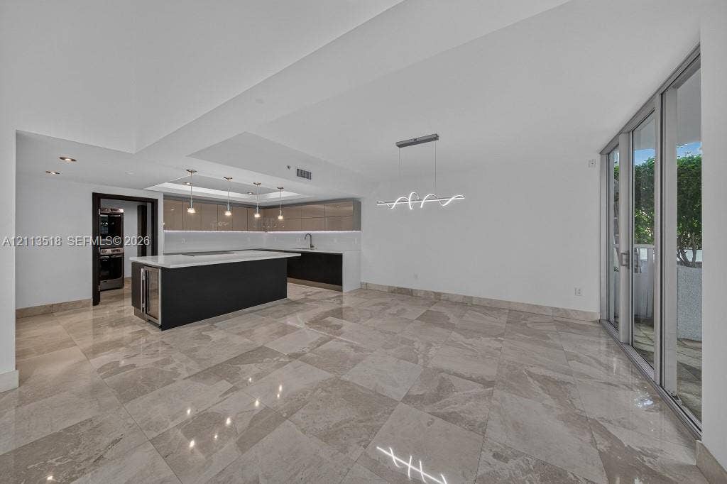 3131 NE 188th Street, #1-303, Aventura, FL 33180 Open-concept area featuring oversized neutral-toned tile flooring, sleek flat-panel cabinetry, a central kitchen island with a stone-finish countertop, minimalist pendant lighting, and floor-to-ceiling glass sliding doors