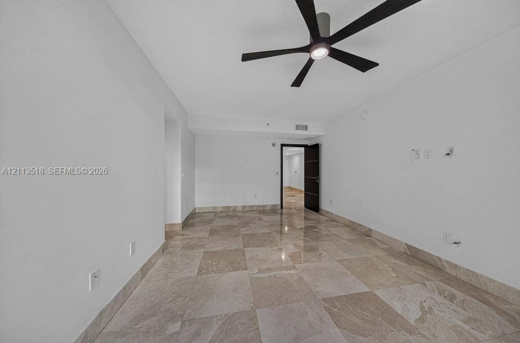 3131 NE 188th Street, #1-303, Aventura, FL 33180 Spacious room featuring polished large-format stone tile flooring, neutral wall finishes, and a contemporary matte black ceiling fan with integrated lighting