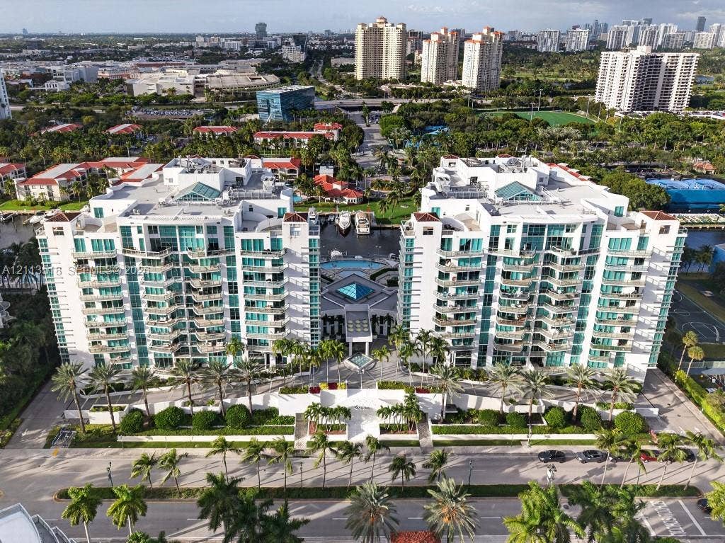 3131 NE 188th Street, #1-303, Aventura, FL 33180 Aerial view of a multi-story residential complex featuring private balconies, central outdoor swimming pool, paved entryway, and manicured landscaping with palm trees