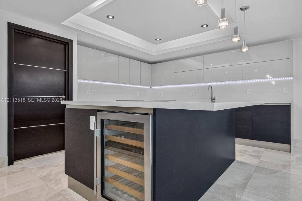 3131 NE 188th Street, #1-303, Aventura, FL 33180 Kitchen featuring high-gloss cabinetry, a central island with a built-in wine refrigerator, stone countertops, recessed tray ceiling lighting, and tile flooring