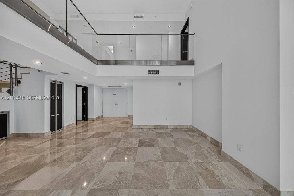 3131 NE 188th Street, #1-303, Aventura, FL 33180 Double-height ceilings with an open mezzanine, glass railing, stone flooring, and recessed lighting