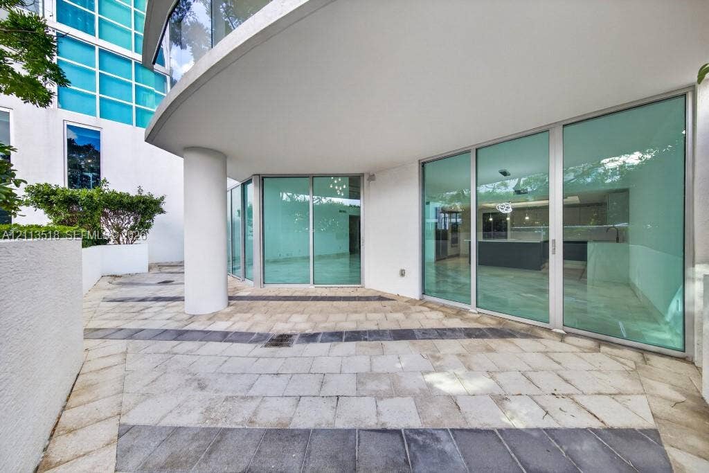 3131 NE 188th Street, #1-303, Aventura, FL 33180 Curved stone patio featuring decorative inlaid tile patterns, expansive floor-to-ceiling glass walls, and a structural concrete support column