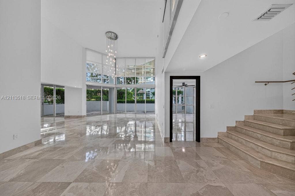 3131 NE 188th Street, #1-303, Aventura, FL 33180 Double-height ceilings, floor-to-ceiling glass wall, polished stone flooring, custom multi-light chandelier, and stone staircase