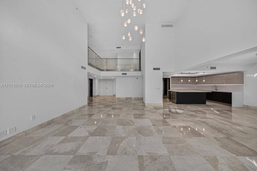 3131 NE 188th Street, #1-303, Aventura, FL 33180 Expansive interior featuring high ceilings, stone flooring, a multi-tiered glass pendant chandelier, a glass-railed mezzanine, and kitchen cabinetry with integrated lighting