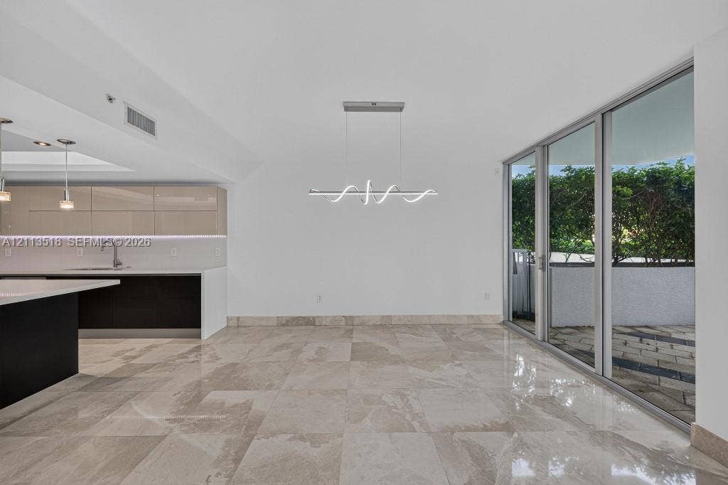 3131 NE 188th Street, #1-303, Aventura, FL 33180 Open-concept interior featuring large-format tile flooring, high-gloss cabinetry, a quartz waterfall island, modern linear architectural lighting, and floor-to-ceiling glass sliding doors