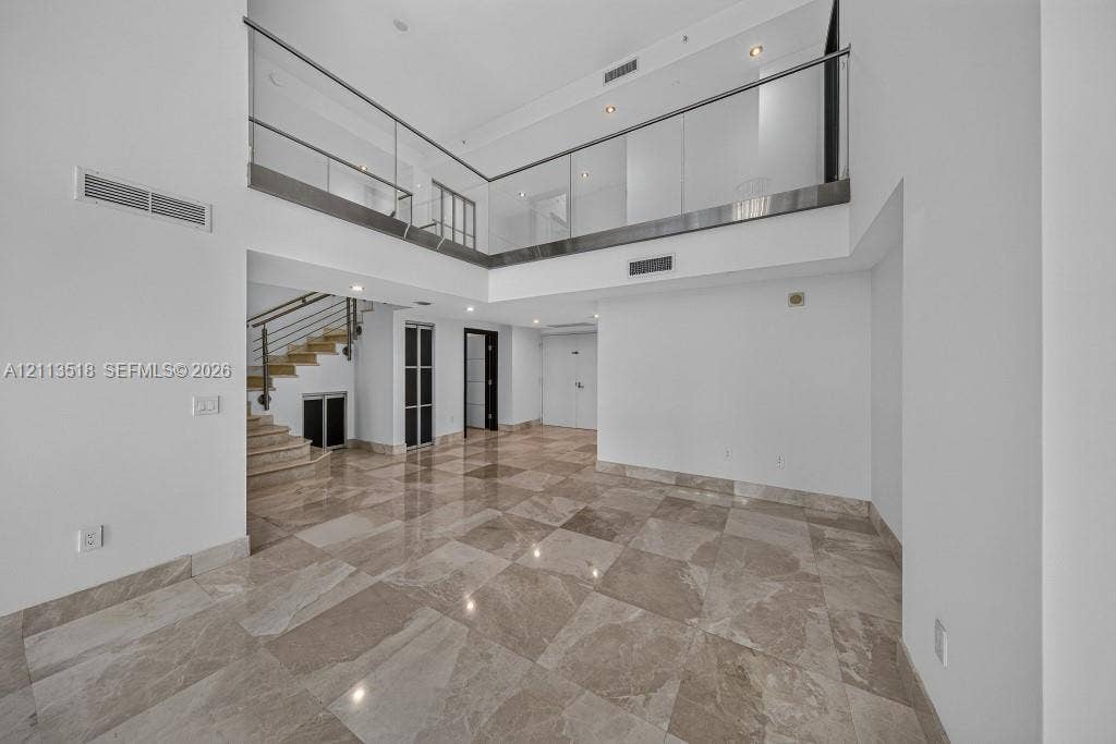 3131 NE 188th Street, #1-303, Aventura, FL 33180 Double-height ceiling, polished stone flooring, glass panel mezzanine railing, recessed lighting, and staircase with metal handrail