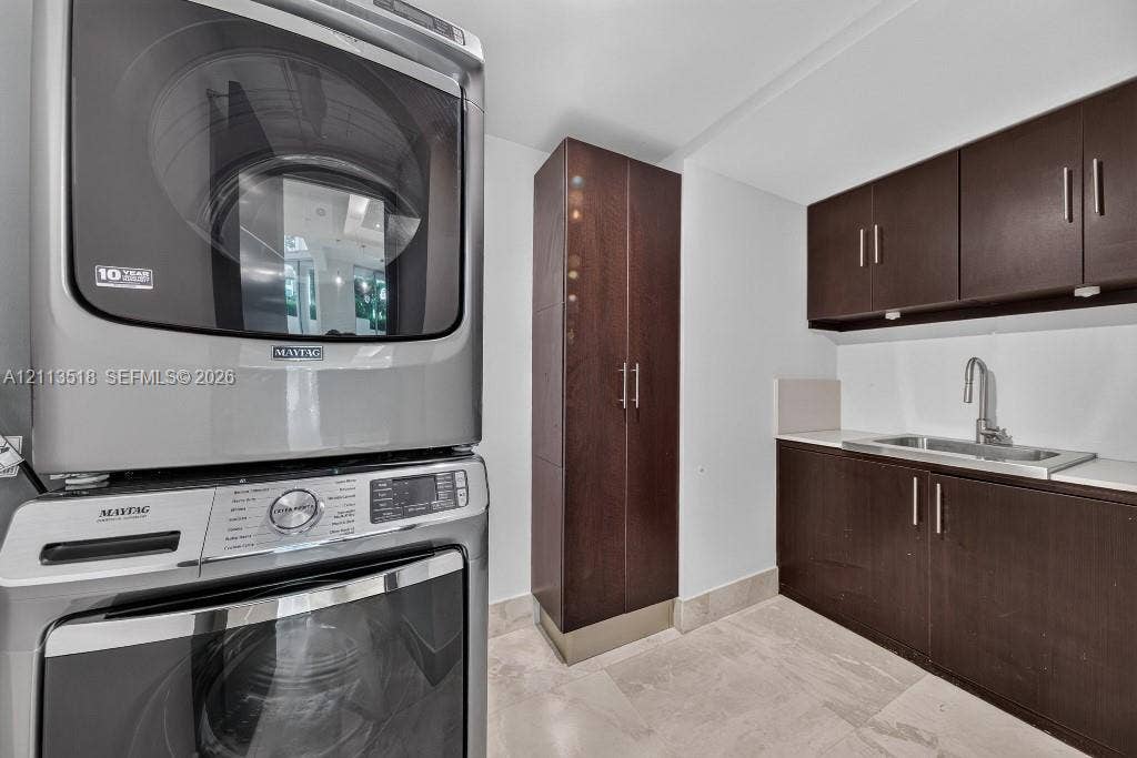 3131 NE 188th Street, #1-303, Aventura, FL 33180 Stacked high-efficiency metallic laundry center, custom dark wood-finish cabinetry, floor-to-ceiling storage pantry, stainless steel undermount sink with a gooseneck faucet, and stone-finish flooring