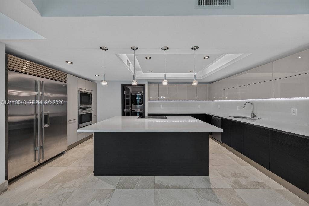 3131 NE 188th Street, #1-303, Aventura, FL 33180 Modern kitchen featuring a central island with a stone countertop, high-gloss cabinetry, stainless steel refrigerator, recessed ceiling lighting, and tile flooring
