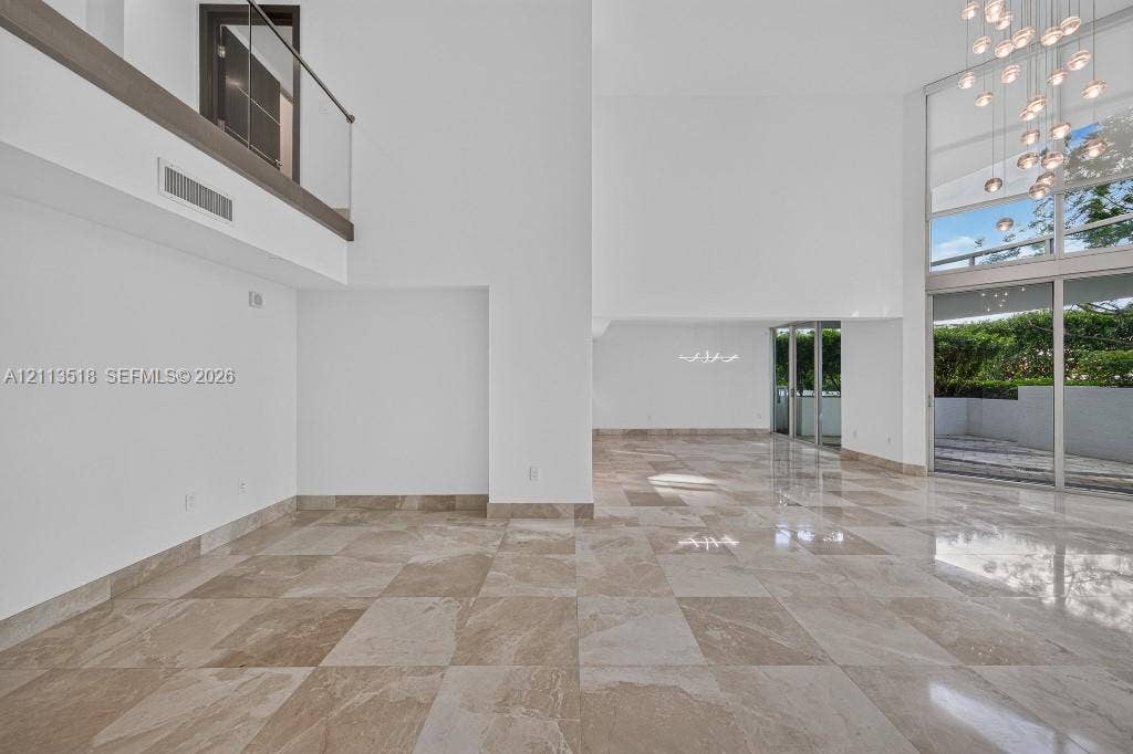3131 NE 188th Street, #1-303, Aventura, FL 33180 Double-height ceilings featuring floor-to-ceiling windows, polished stone flooring, a multi-pendant chandelier, and a glass-paneled mezzanine railing