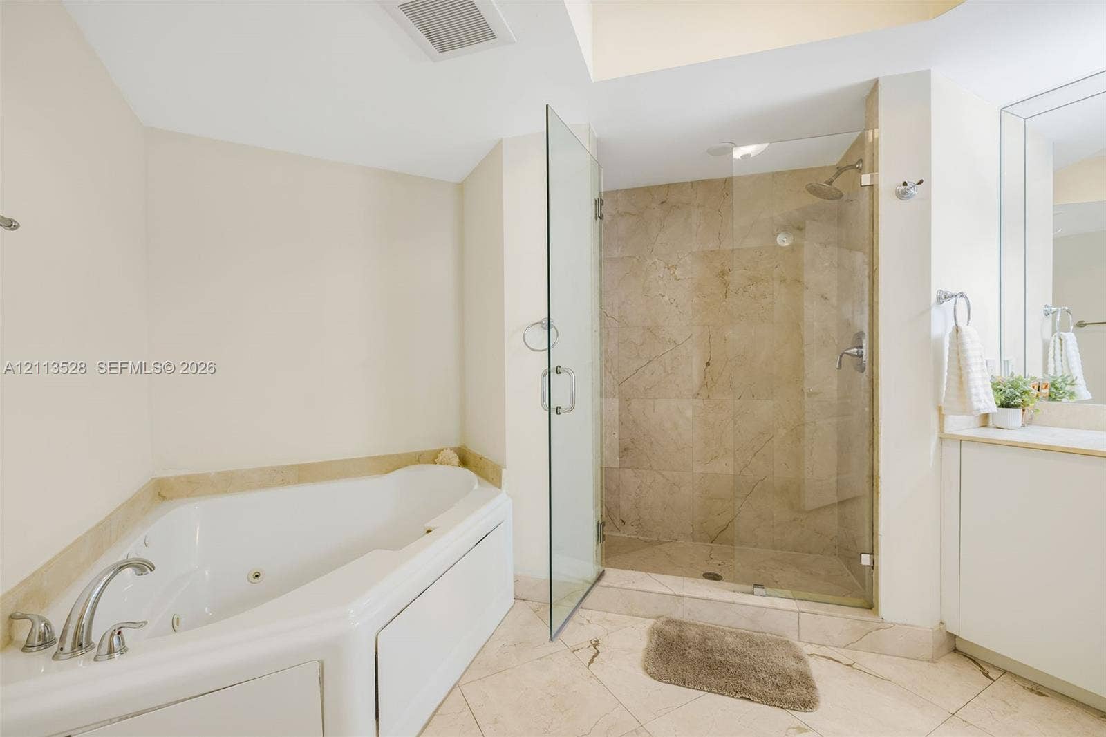 17555 Atlantic Boulevard, #1108, Sunny Isles Beach, Sunny Isles Beach, FL 33160 Jetted soaking tub, walk-in shower with stone-tile surround, frameless glass enclosure, stone flooring, and built-in vanity