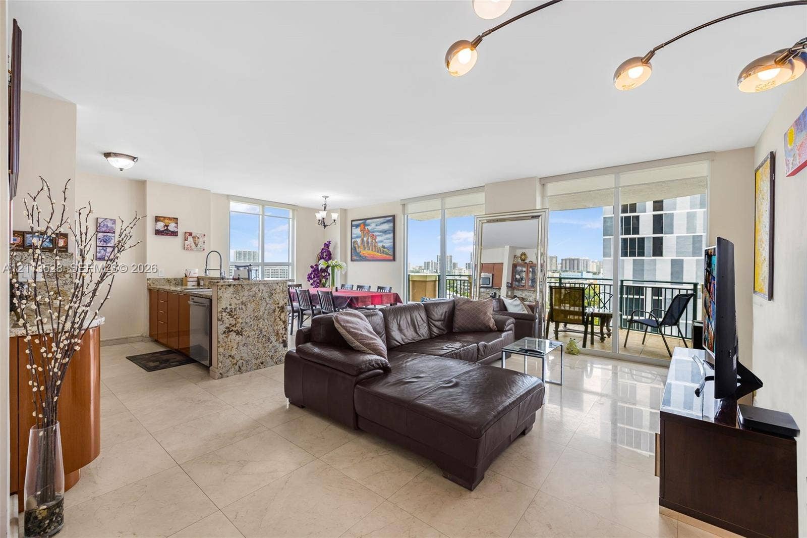 17555 Atlantic Boulevard, #1108, Sunny Isles Beach, Sunny Isles Beach, FL 33160 Open-concept interior featuring light-toned tile flooring, floor-to-ceiling glass balcony doors, kitchen island with stone-surface countertop, and multi-arm statement lighting