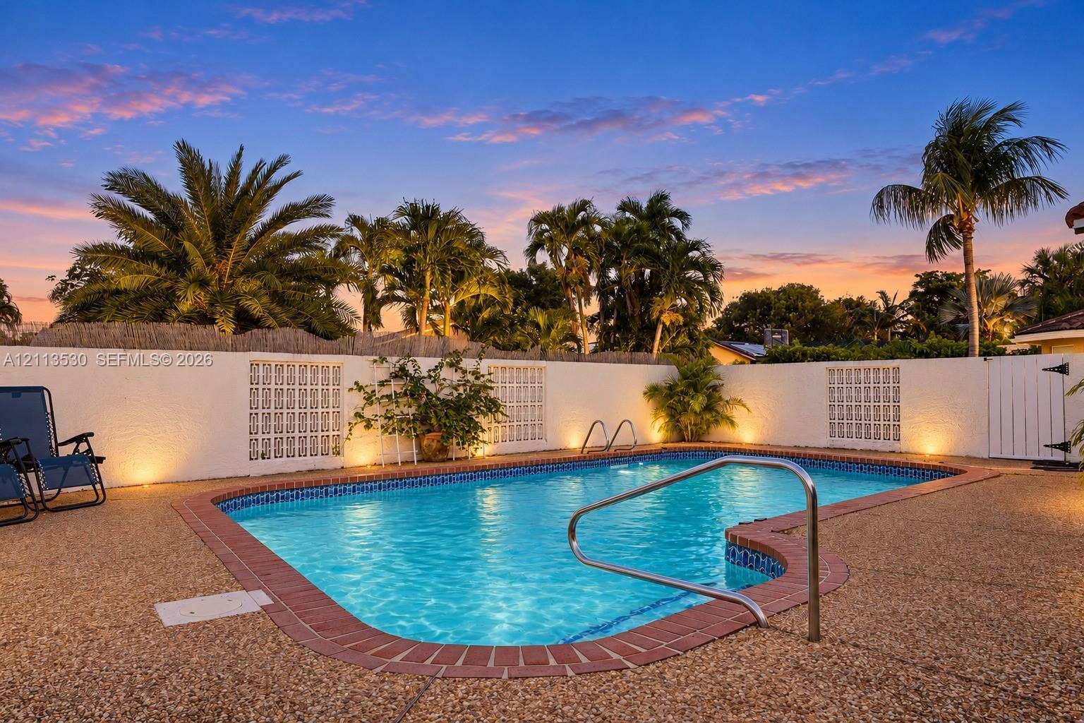 1773 NW 82nd Avenue, Coral Springs, FL 33071 In-ground swimming pool featuring a brick-tiled coping edge, a metal handrail, and a textured stone-finish patio surround enclosed by a masonry privacy wall with decorative lattice panels