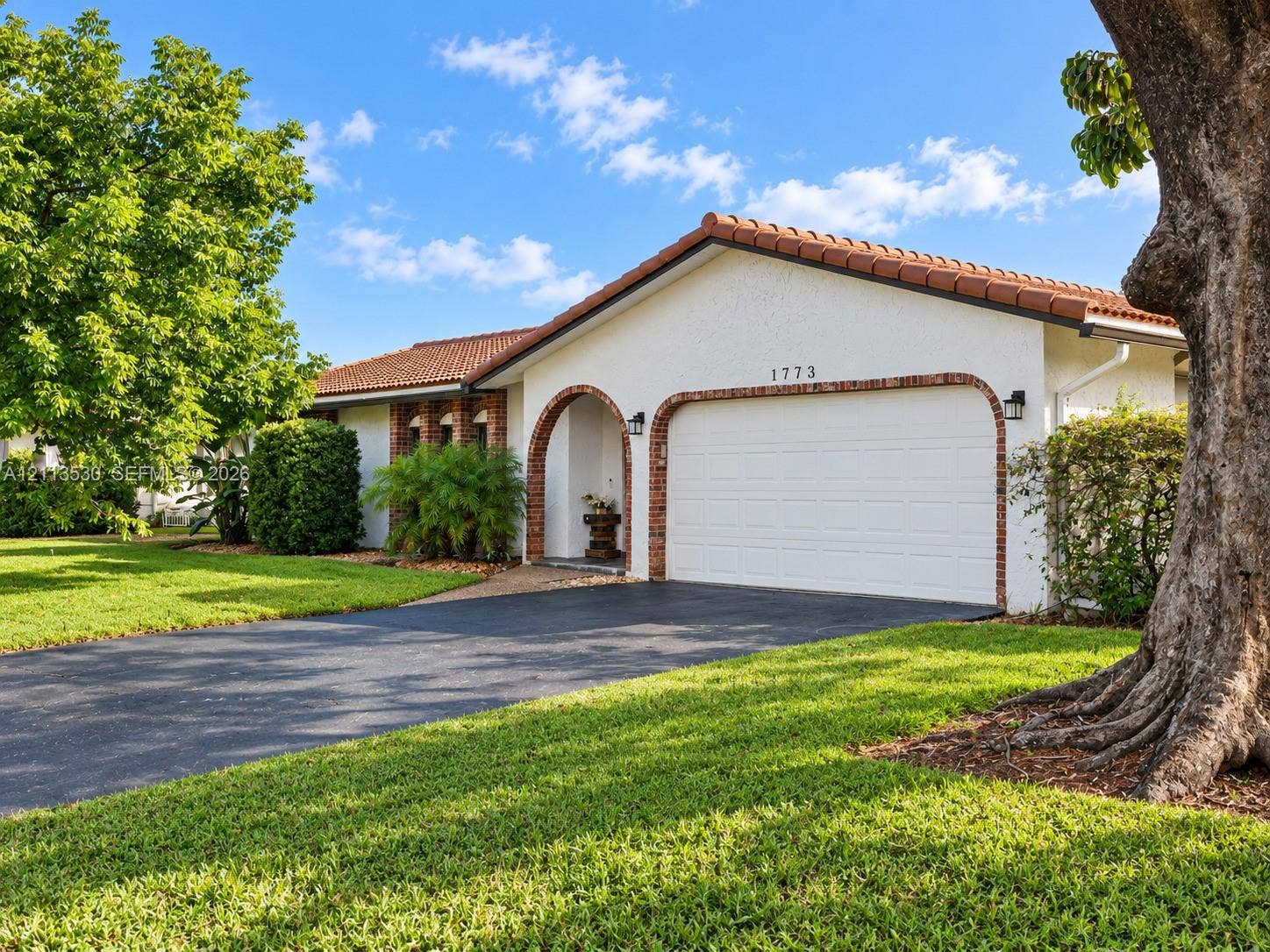 1773 NW 82nd Avenue, Coral Springs, FL 33071 Stucco exterior residence featuring a terracotta-tiled roof, arched entryway, brick masonry detailing, and an attached multi-car garage