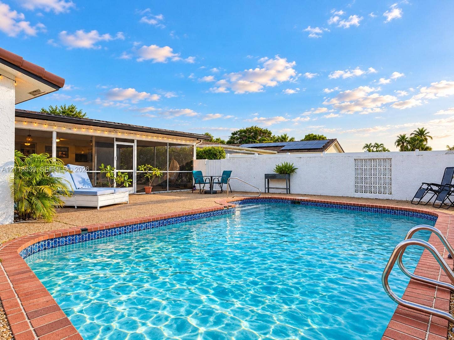 1773 NW 82nd Avenue, Coral Springs, FL 33071 In-ground swimming pool with brick coping, surrounded by a textured aggregate patio and enclosed by a masonry privacy wall featuring integrated glass block accents, complemented by a screened-in lanai