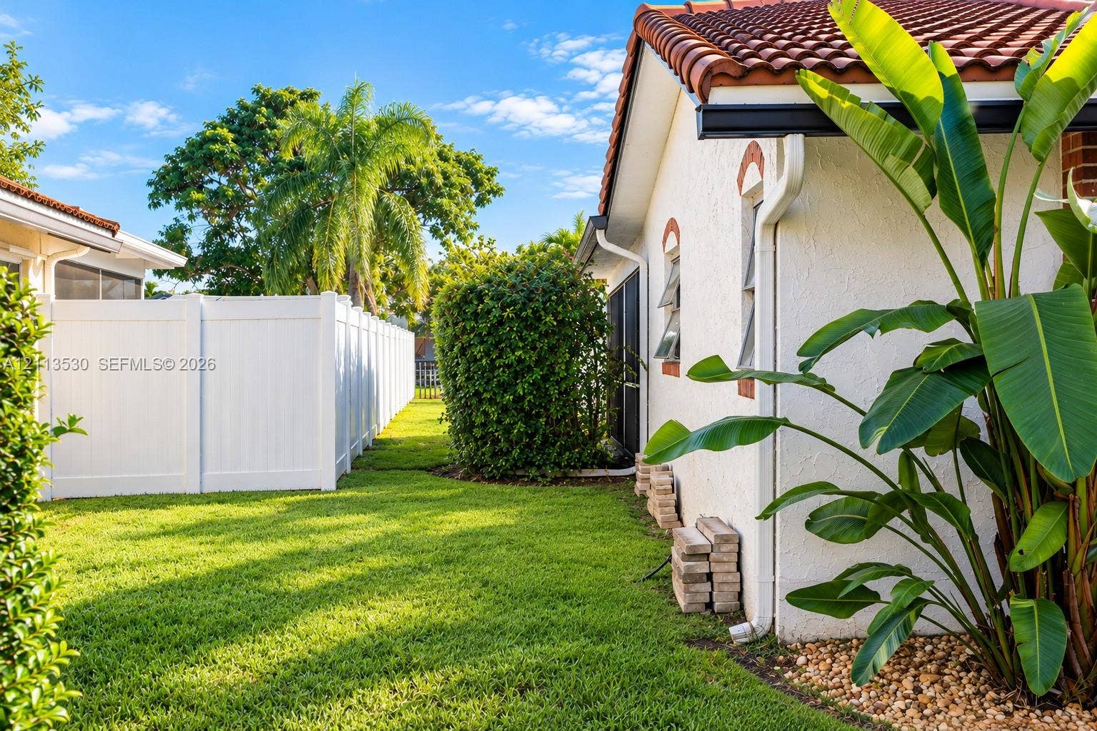 1773 NW 82nd Avenue, Coral Springs, FL 33071 Stucco exterior with terracotta-style clay tile roofing, white vinyl privacy fencing, and landscaped side yard