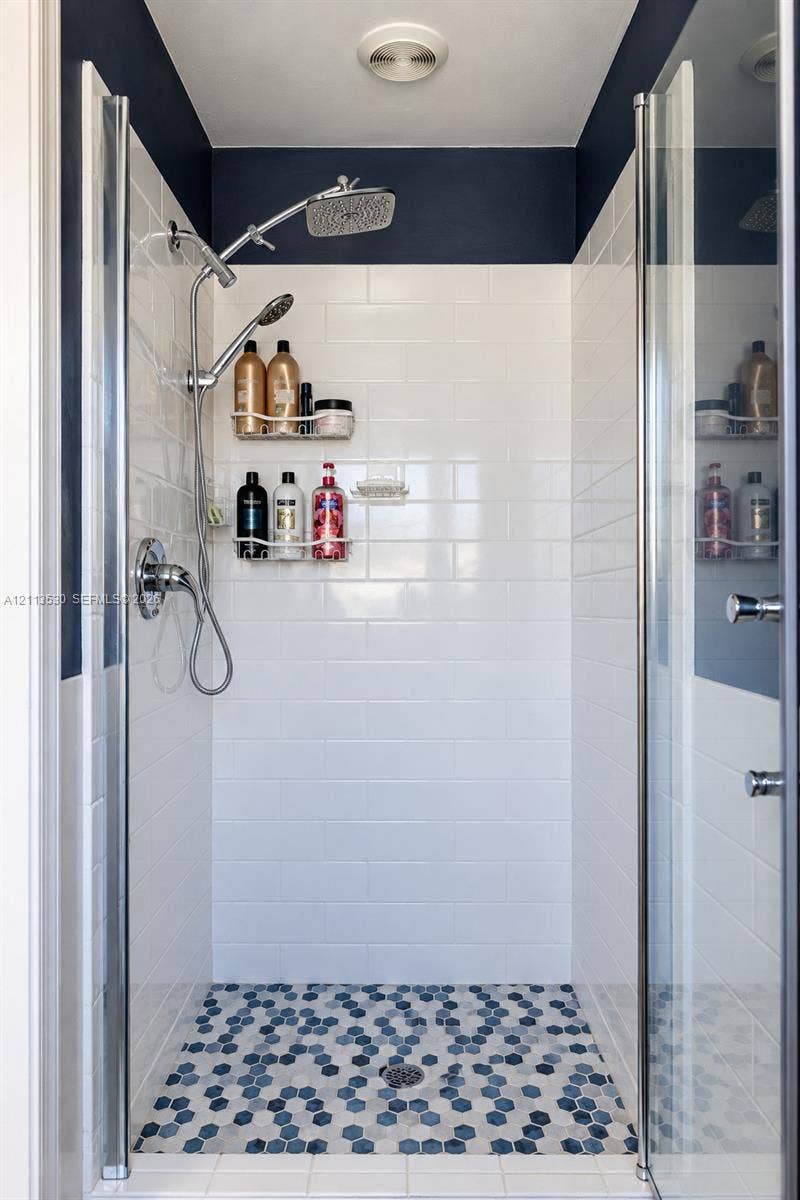 1773 NW 82nd Avenue, Coral Springs, FL 33071 Walk-in shower enclosure featuring white subway tile walls, geometric hexagonal floor tile, chrome rain showerhead with a secondary handheld sprayer, and glass panel doors