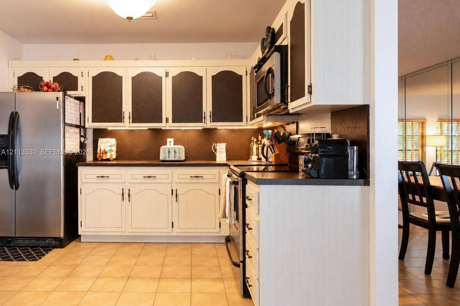 1773 NW 82nd Avenue, Coral Springs, FL 33071 Kitchen featuring custom two-tone cabinetry, solid surface countertops, under-cabinet lighting, stainless steel appliances, and ceramic tile flooring