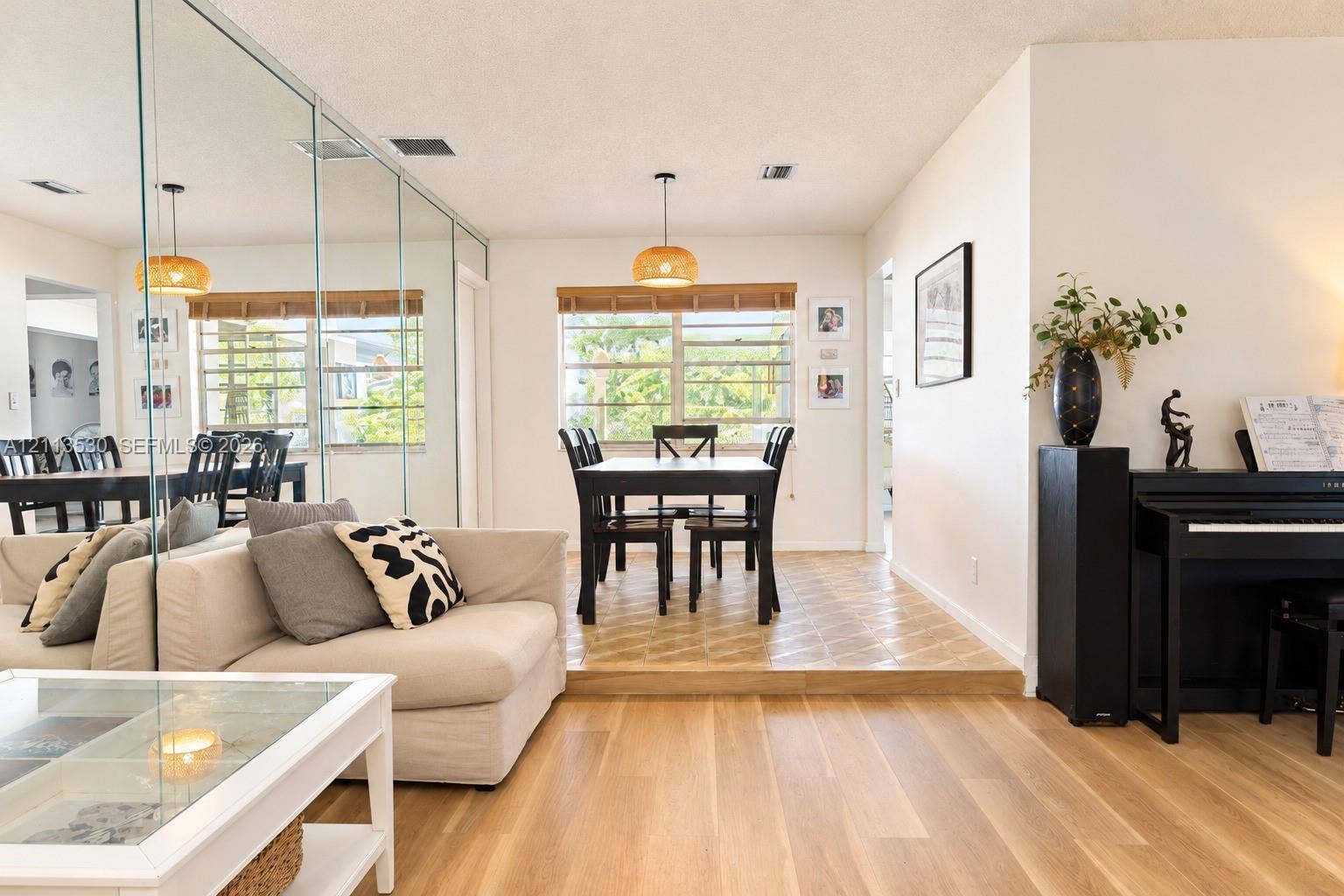1773 NW 82nd Avenue, Coral Springs, FL 33071 Sunlit room featuring wood-finish flooring, a wall-to-wall mirrored accent, tiered floor elevation, and dual pendant light fixtures