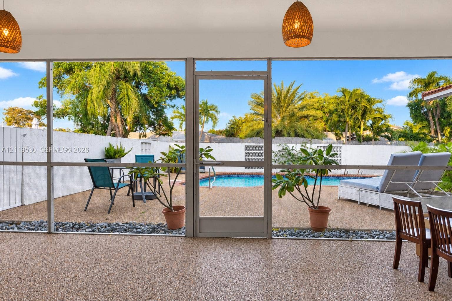 1773 NW 82nd Avenue, Coral Springs, FL 33071 Screen-enclosed patio with textured aggregate flooring, dual woven-texture pendant light fixtures, and a direct entrance to an outdoor swimming pool area featuring a perimeter privacy wall