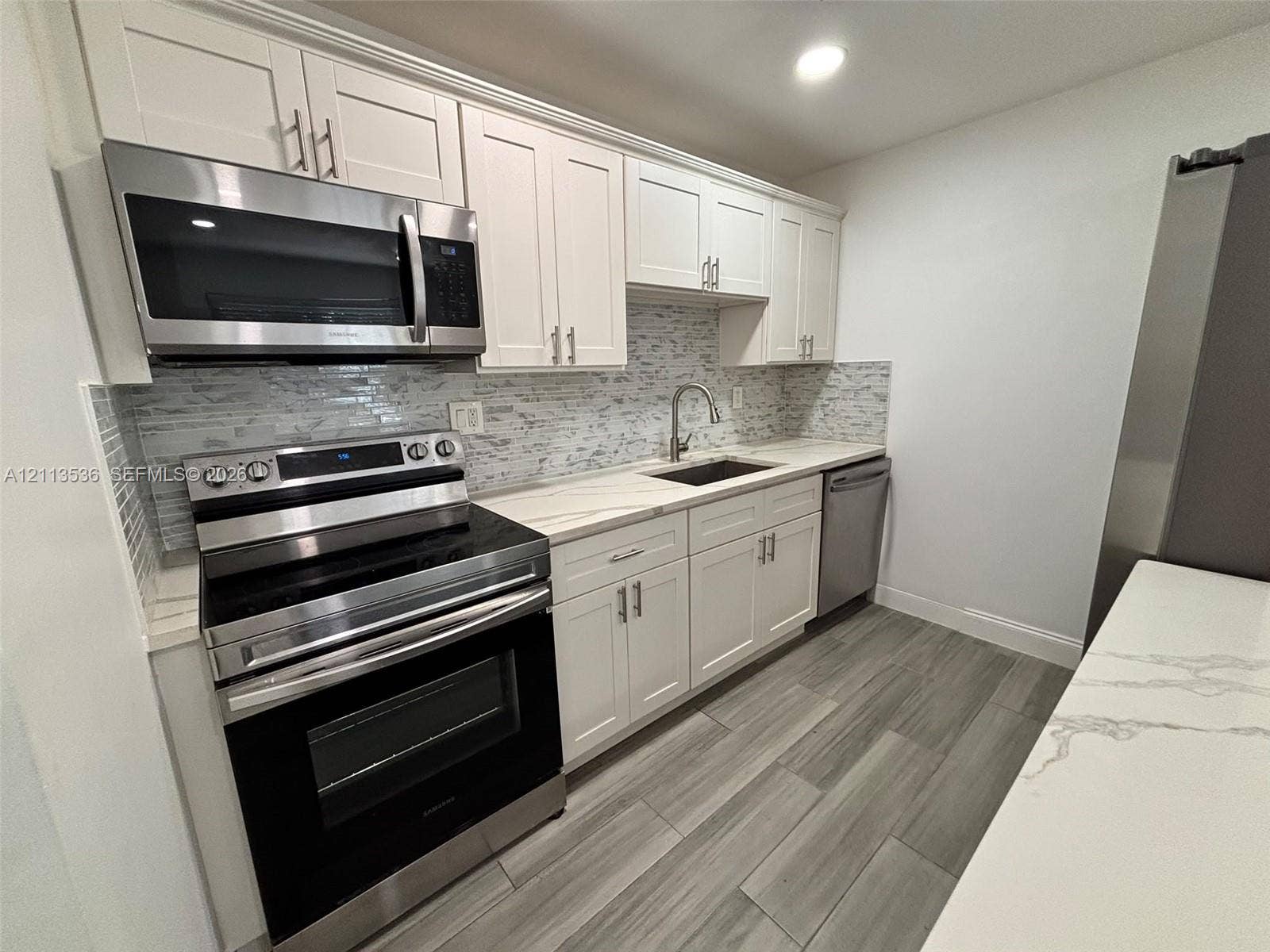 4840 SW 25th Avenue, #4840, Dania, Dania Beach, FL 33312 Kitchen featuring white Shaker-style cabinetry, stainless steel appliances, quartz countertops, a stone-tile backsplash, and wood-finish flooring