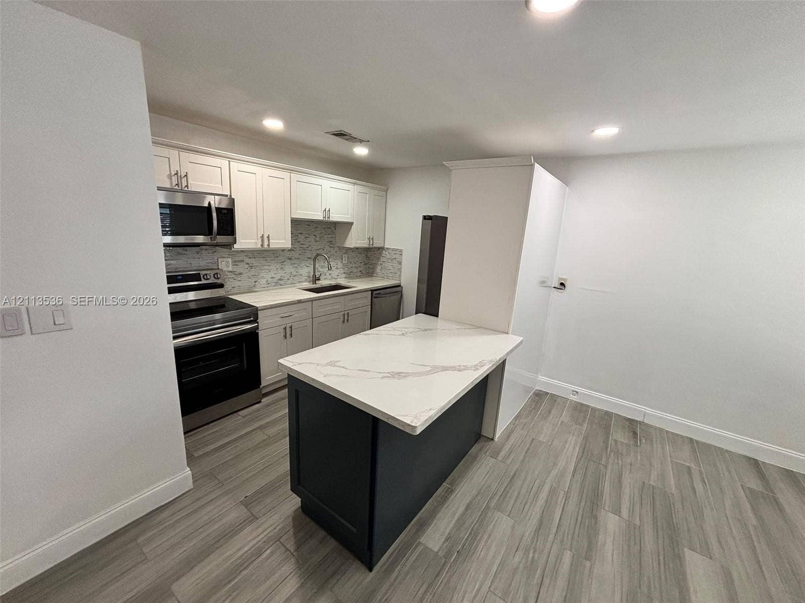 4840 SW 25th Avenue, #4840, Dania, Dania Beach, FL 33312 Kitchen featuring white cabinetry, an island with a stone-composite countertop, stainless steel appliances, a tile backsplash, and wood-finish flooring