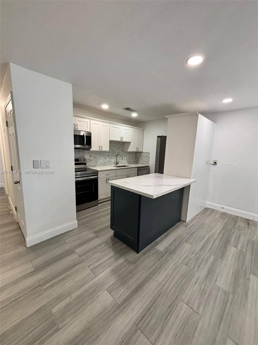 4840 SW 25th Avenue, #4840, Dania, Dania Beach, FL 33312 Kitchen featuring white cabinetry, stone-finish countertops, a contrasting dark-finish kitchen island, stainless steel appliances, and wood-finish flooring