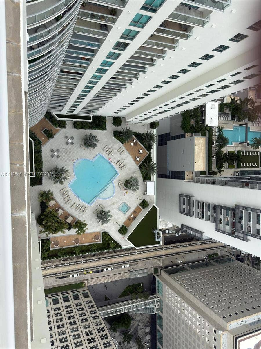 Aerial perspective of a high-rise exterior featuring a paved pool deck, custom-shaped swimming pool, built-in spa, and landscaped greenery