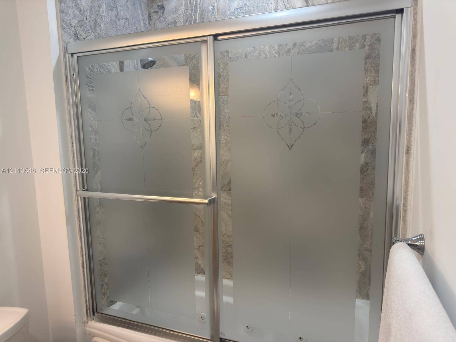 Shower enclosure featuring a metal-framed bypass door with etched glass detailing and stone-tile surround