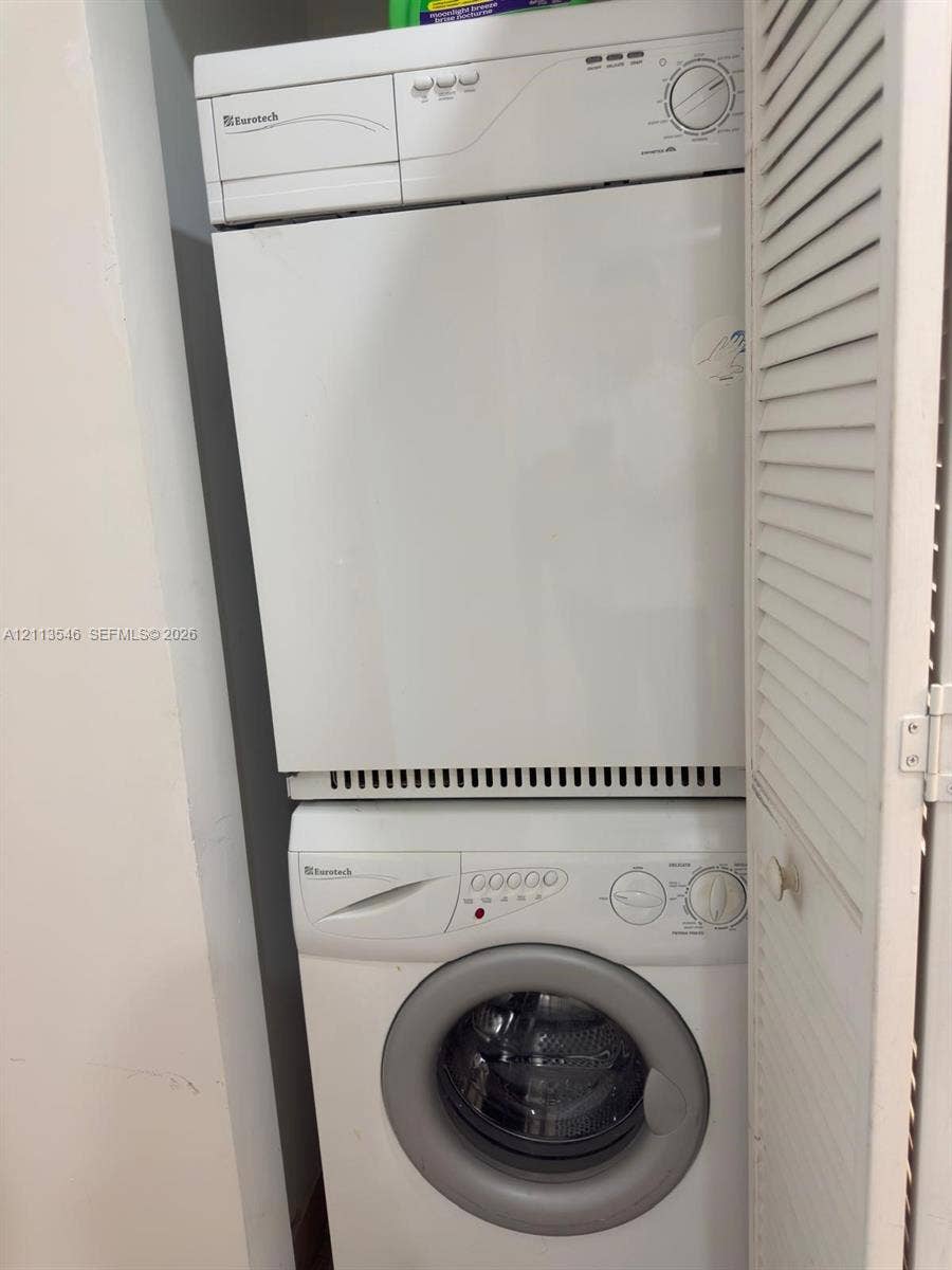 Stacked laundry center featuring a front-loading washer and louvered closet doors