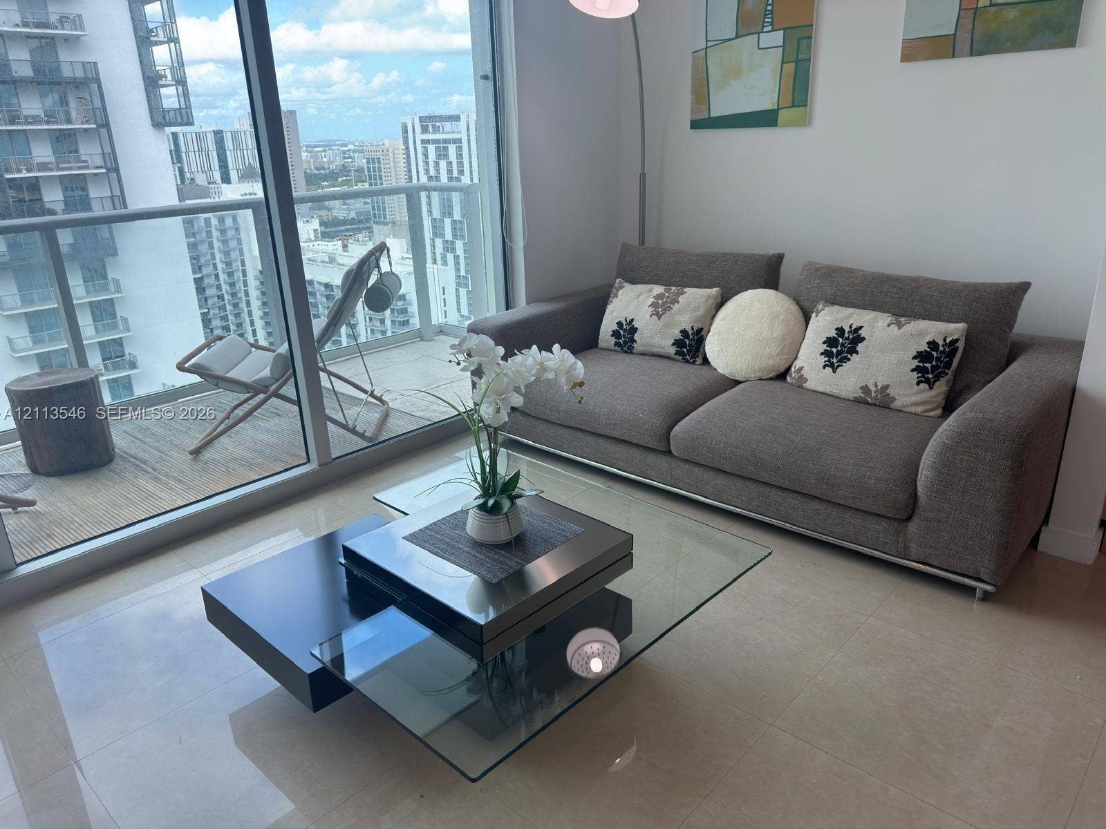 Floor-to-ceiling glass doors, neutral tile flooring, and a private balcony featuring a glass panel railing