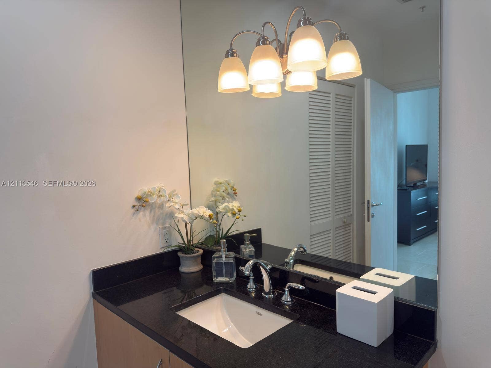 Vanity featuring a dark stone countertop, integrated undermount sink, chrome widespread faucet, large-format mirror, and five-light glass shade fixture