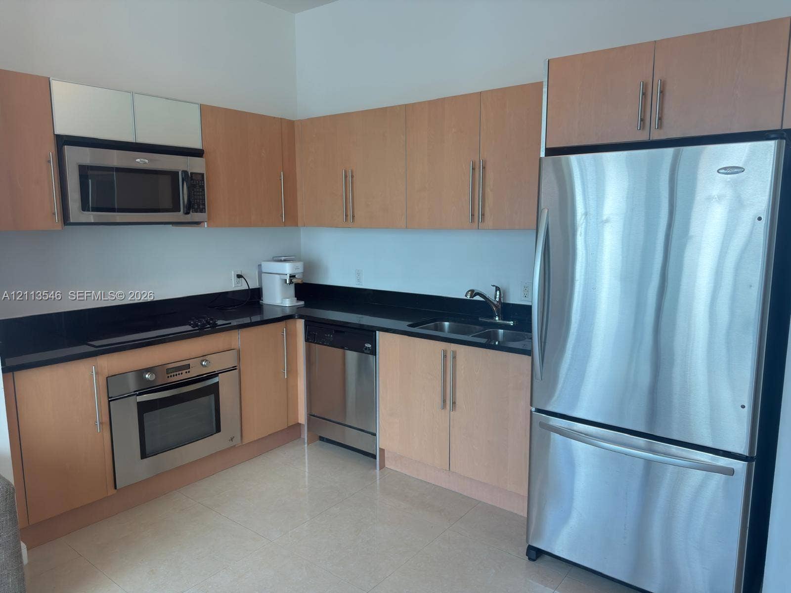 Kitchen featuring light-finish cabinetry, black countertops, stainless steel appliances, a built-in oven, and tile flooring