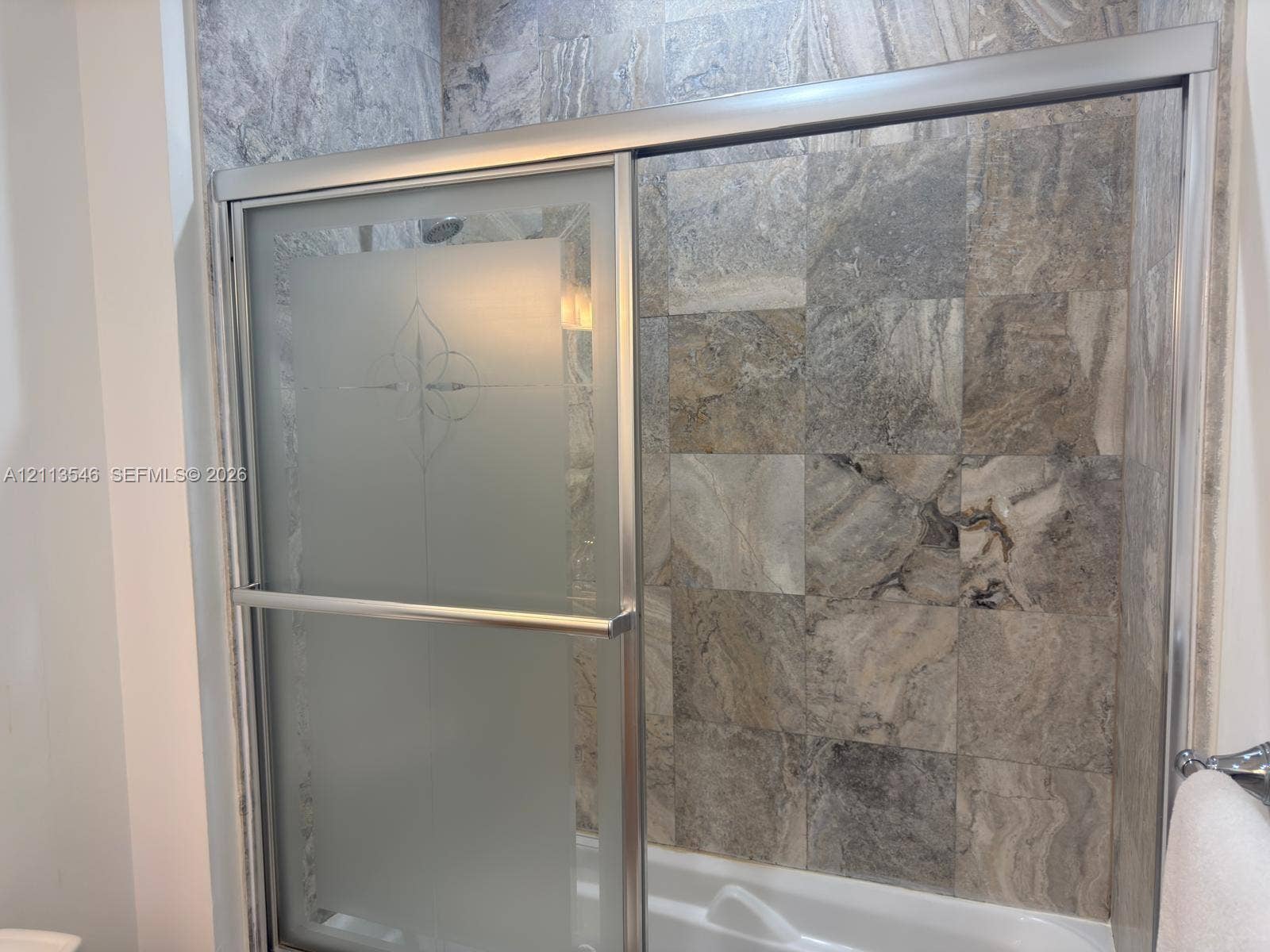 Shower enclosure featuring stone-tile wall surrounds, a sliding glass door with etched detailing, and a metallic frame