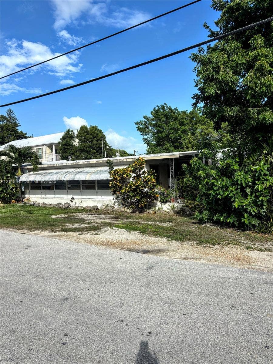 93 1st Court, Key Largo, FL 33037 Exterior featuring a single-story structure with an attached metal awning, decorative metal porch supports, and mature perimeter landscaping