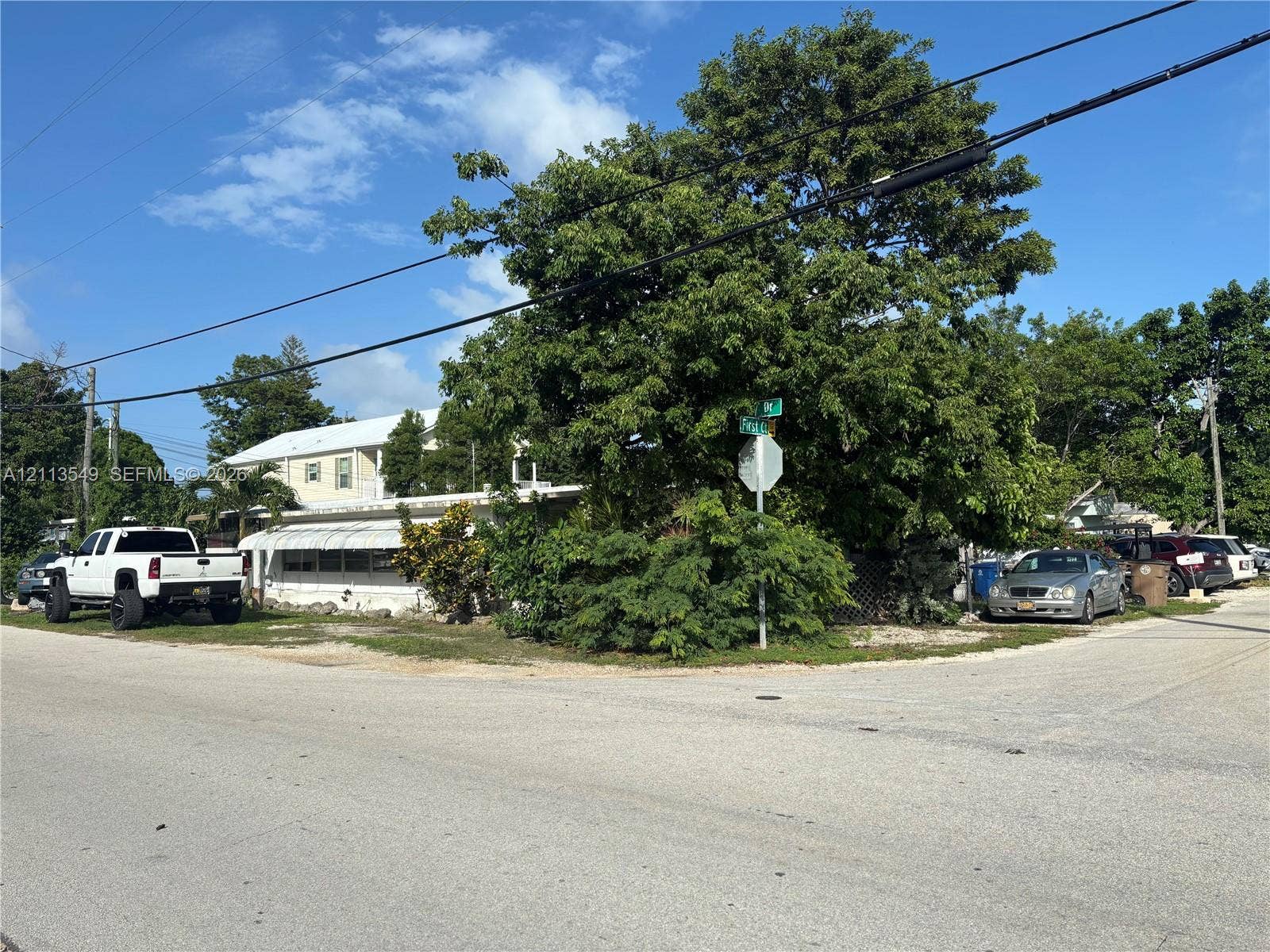 93 1st Court, Key Largo, FL 33037 Corner lot featuring light-colored exterior siding, an expansive awning, and established mature trees