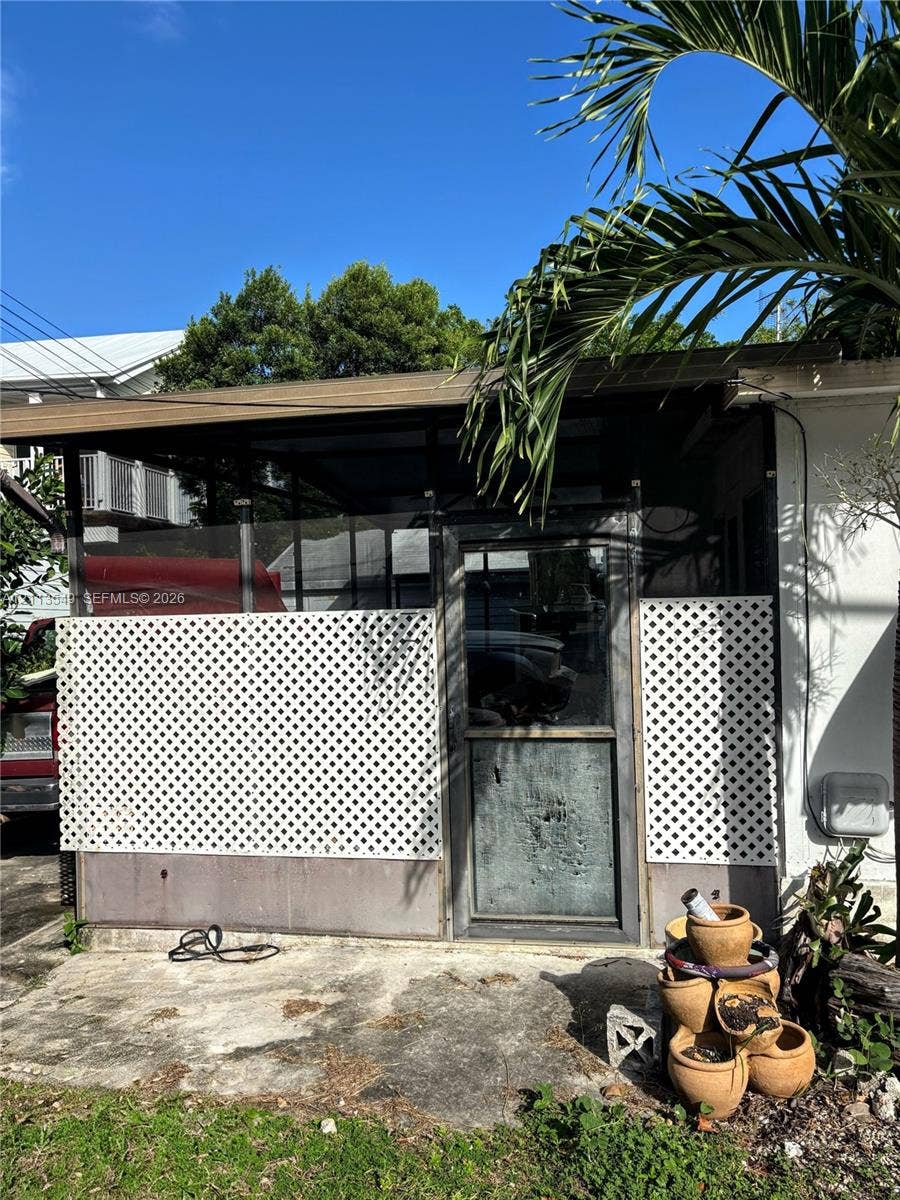 93 1st Court, Key Largo, FL 33037 Enclosed porch featuring metal framing, diamond-pattern lattice panels, a glass-pane door, and a concrete patio foundation