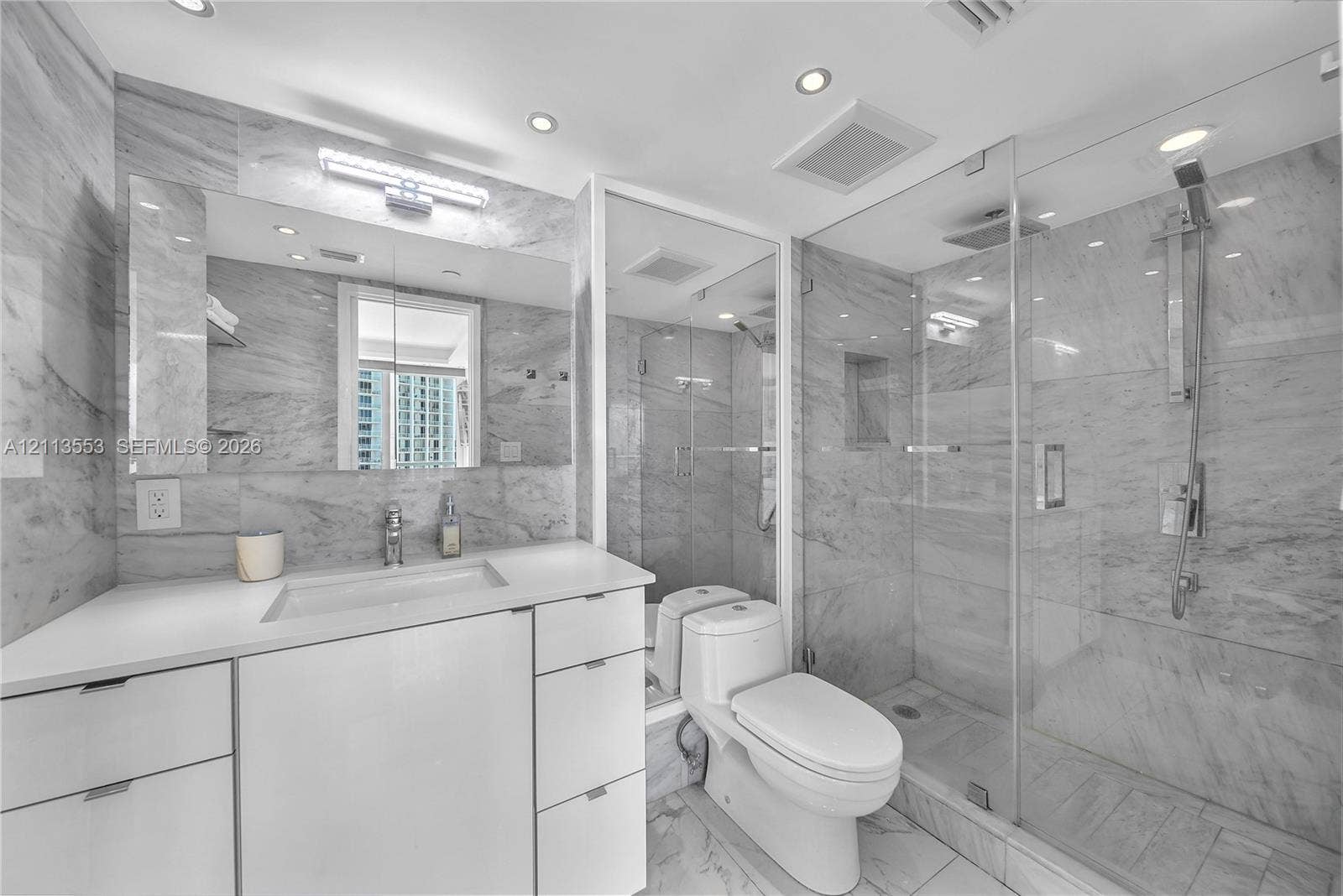 400 S Pointe Drive, #2106, Miami Beach, FL 33139 Bathroom featuring large-format stone wall tiling, white cabinetry with a solid-surface countertop, glass-enclosed walk-in shower with rainfall showerhead, and recessed ceiling lighting