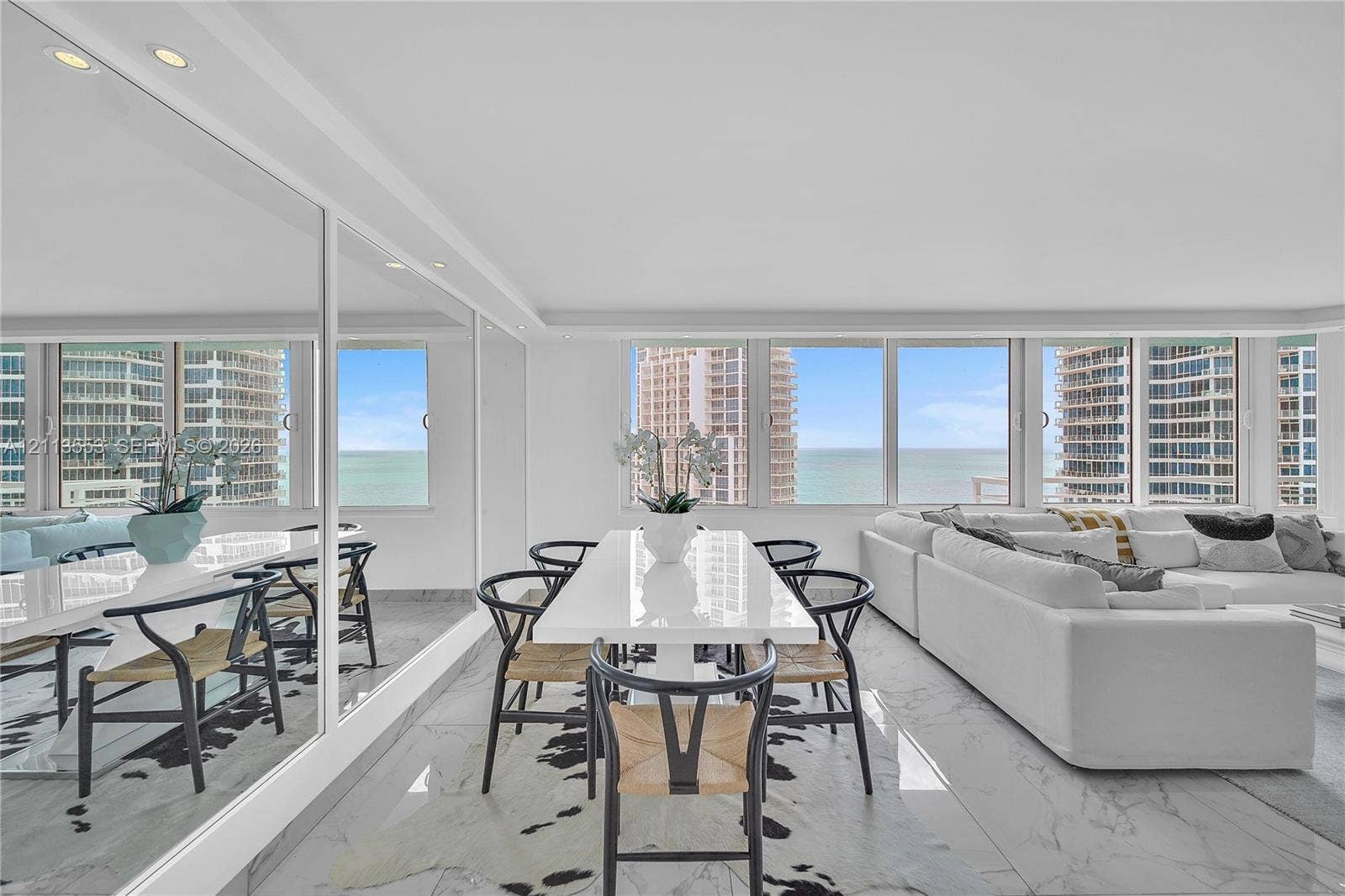 400 S Pointe Drive, #2106, Miami Beach, FL 33139 Open-concept living space featuring floor-to-ceiling windows, polished stone flooring, and expansive wall-mounted mirrors with integrated recessed lighting